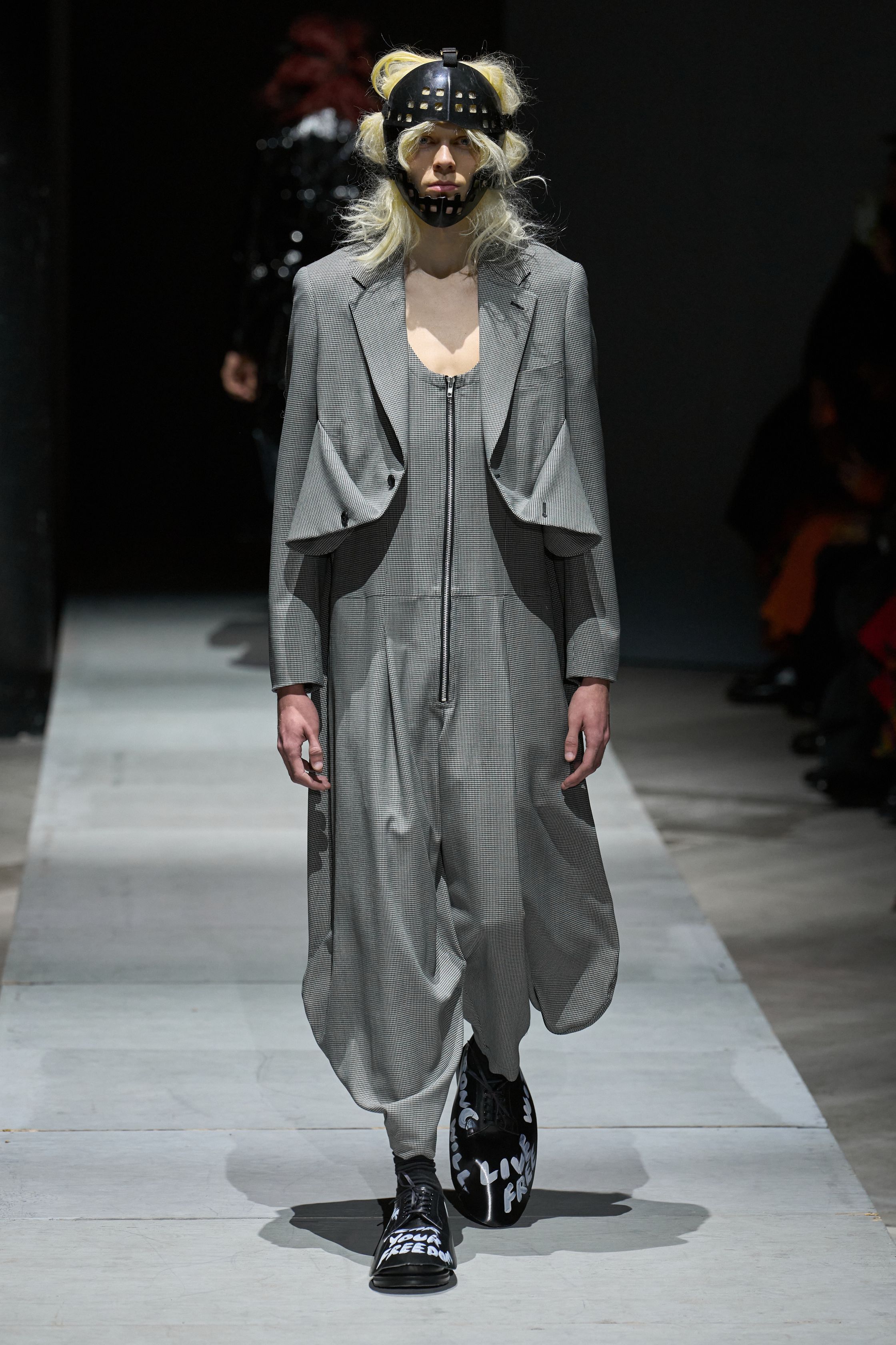 Comme des Garçons Homme Plus 2026秋冬以极端造型继续挑战“男性身体”的社会想象。面具、假发、解构西装与异化比例营造出近乎仪式化的压迫氛围，黑白灰成为思想载体而非装饰。这是一场关于权力、恐惧与集体意识的时装实验，服装不再服务于穿着，而是成为观念的武器-顽石频道趋势研究